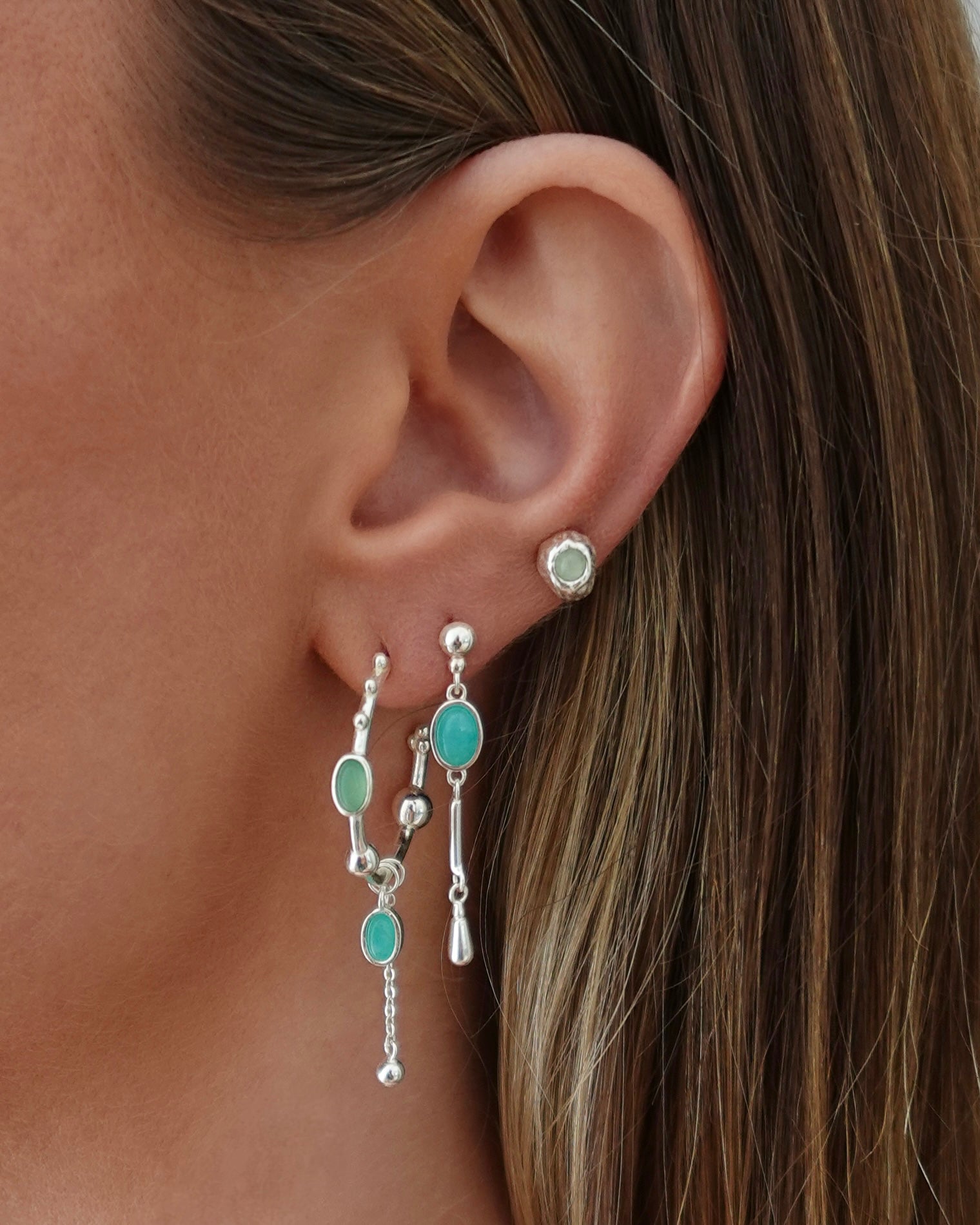 Close-up of an ear wearing a turquoise earring with a chain detail.