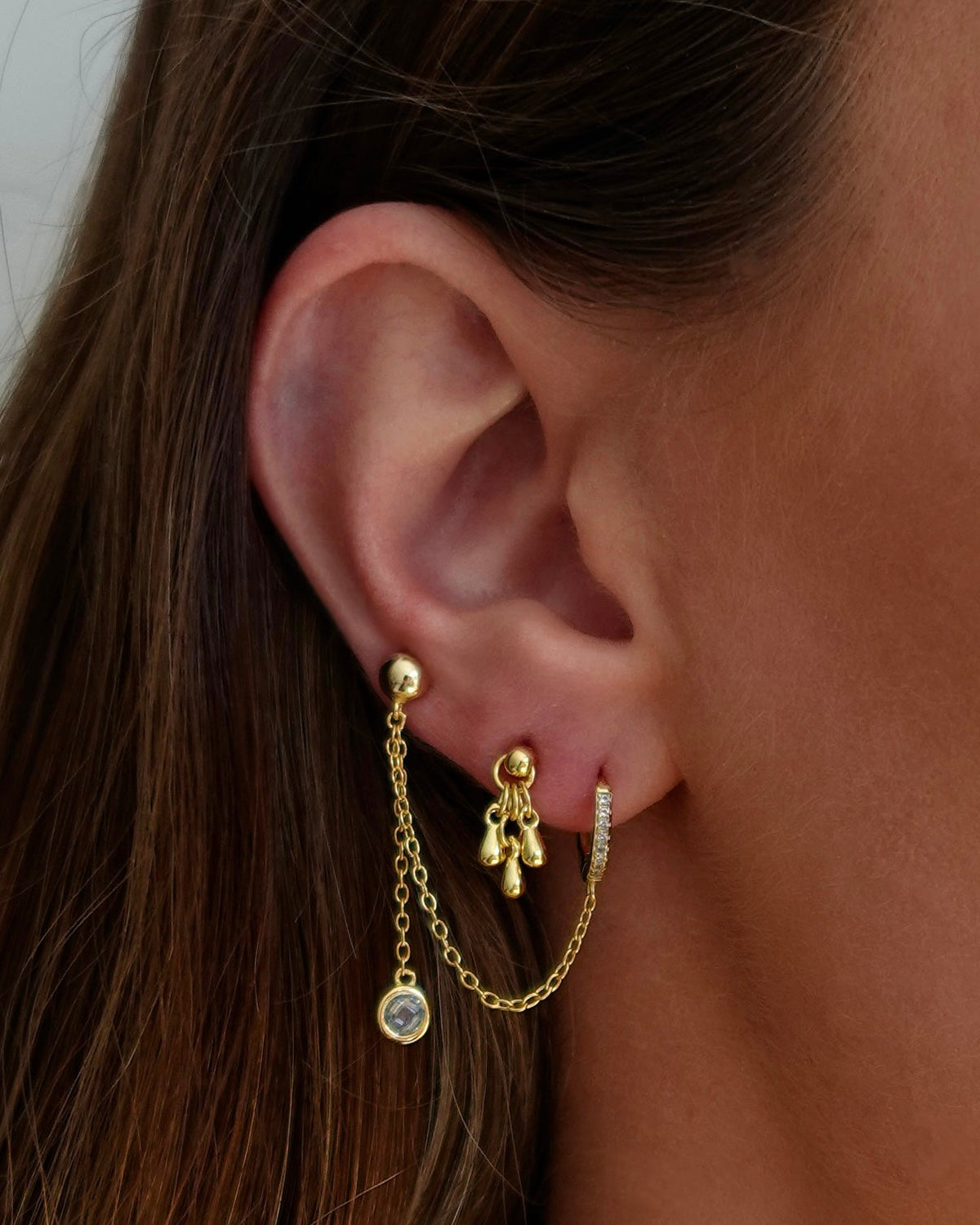 Close-up of an ear wearing gold earrings with chain and gemstone details.