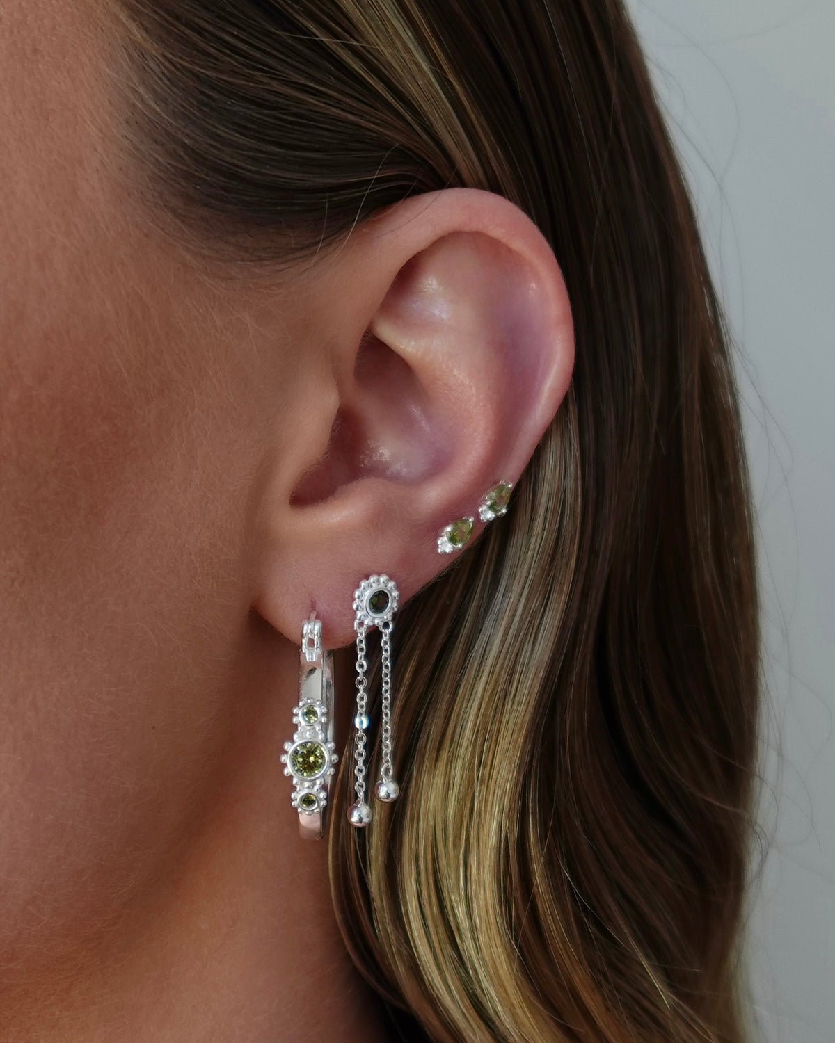 Close-up of an ear wearing multiple earrings with a neutral background